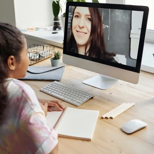 Young girl uses her home computer to have a videoconference with her teacher.