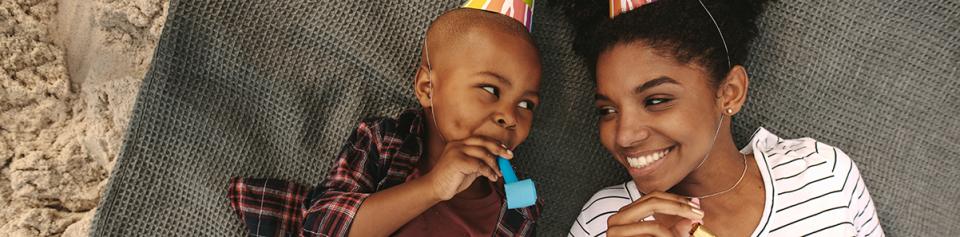 Brother and sister in party hats play with party favors on the floor.