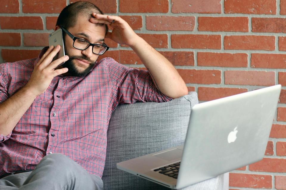 Frustrated man on phone, looking at laptop.