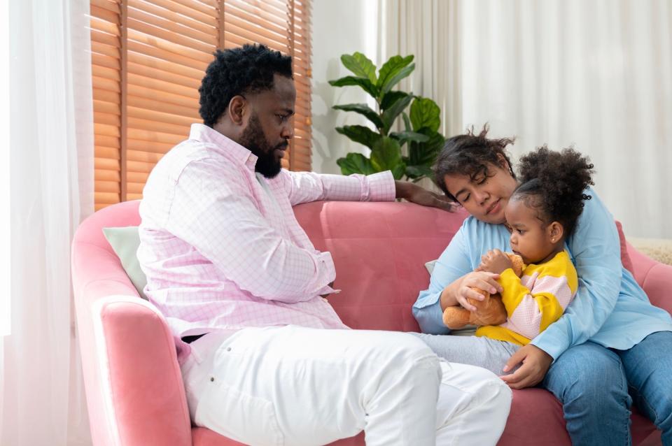 Dad and mom talking to young daughter on couch. 