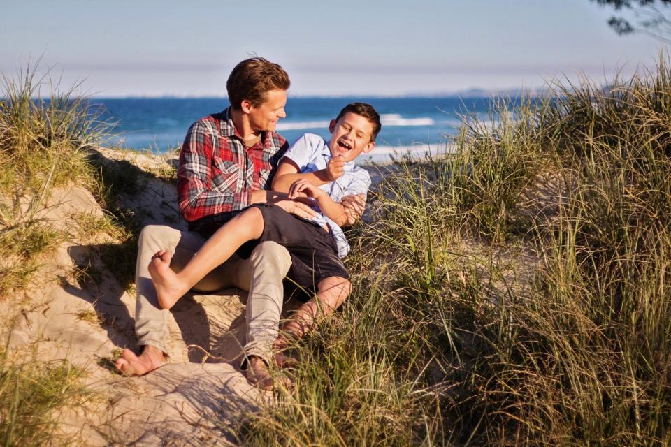 Dad and son laughing on the beach. 