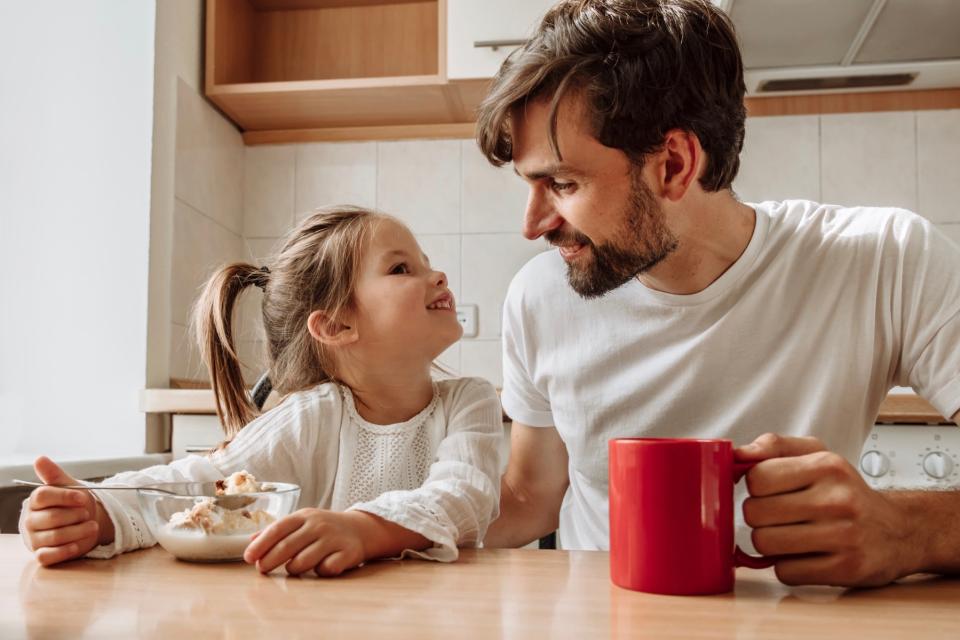 Man and young girl sitting at the kitchen table smiling.